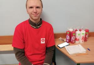 Uczeń zbierający datki na cele charytatywne, przy stoisku ze świecami "Caritas"