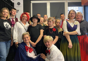 Grupa uczniów z nauczycielkami w strojach gotowa do występu.