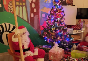 Zdjęcie przedstawia Świętego Mikołaja przy choince
