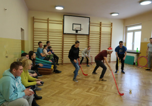 Wolontariusze grają z uczniami w unihokeja.