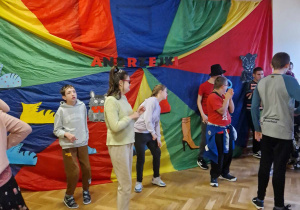 Zabawa Andrzejkowa. Uczniowie tańczą na tle kolorowej chusty animacyjnej.