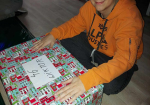 Uśmiechniety chłopiec siedzi na podłodze ze swoim prezentem.