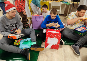 Trzech chłopców siedzac na podłodze, ogląda swoje prezenty.
