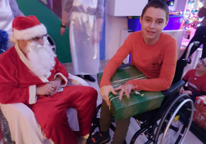 Niepełnosprawny chłopiec na wózku odbiera prezent od św. Mikołaja.