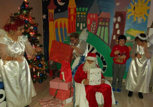 Św Mikołaj i wychowawcy-anioły, przekazują chłopcu prewzent.