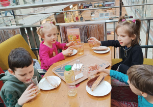 czworo przedszkolaków przy stoliku w kawiarni , degustują ciasta i sok