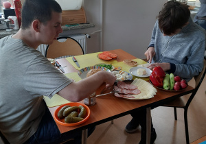 chłopcy robia przy stole kanapki z serów , wędlin i warzyw
