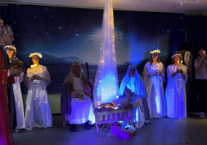 Uczniowie i nauczyciele w strojach aniołów wokół żłóbka.