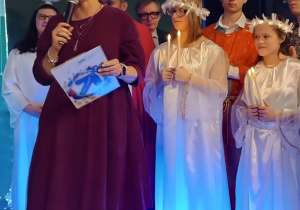 Przemówienie pani dyrektor , w tle osoby w strojach aniołów