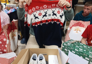 Dziewczynka prezentuje otrzymany w prezencie swetr. W tyle widoczne dzieci z prezentami