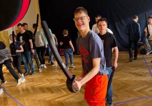 Na zdjęciu widać ucznia w czerwonych spodniach, ćwiczącego uderzanie pałaszem na tarczę.