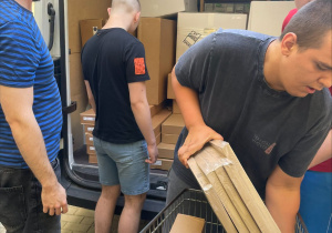 Uczniowie wypakowują paczki z meblami IKEA z samochodu dostawczego.